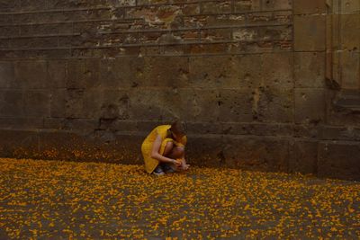 Woman sitting on yellow wall