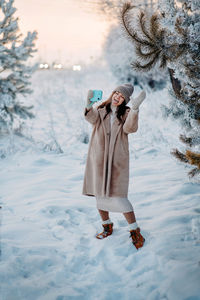 A girl in a beige faux fur coat tooks selfie in a snowy forest. beautiful fairy winter in the forest