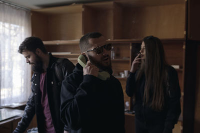 Man talking on telephone while woman smoking cigarette with friend at home