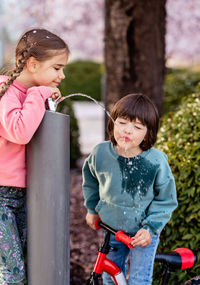 Little children having fun drinking from water fountain in spring park outdoors. carefree childhood