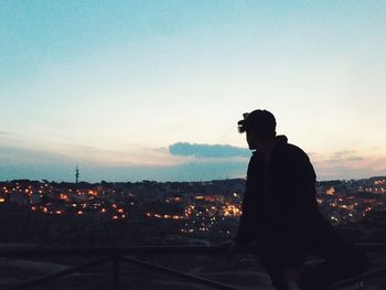 Silhouette man looking at cityscape against sky during sunset