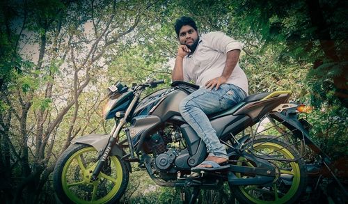 Portrait of young man sitting on bicycle against trees