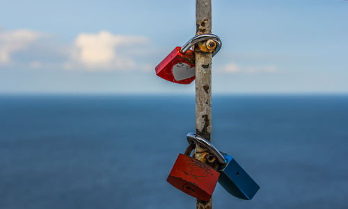 Close-up of padlocks hanging on pole against sea