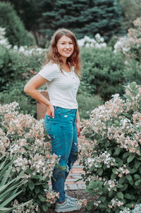 Portrait of smiling young woman standing by flowering plants