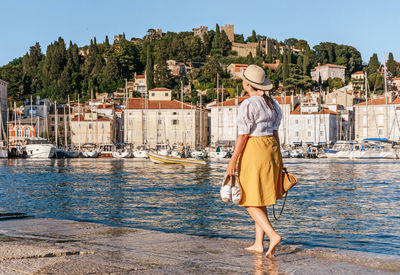 Rear view of woman walking in marina with sailing boats moored in idyllic seaside town