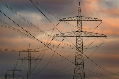 Low angle view of electricity pylon against sky during sunset