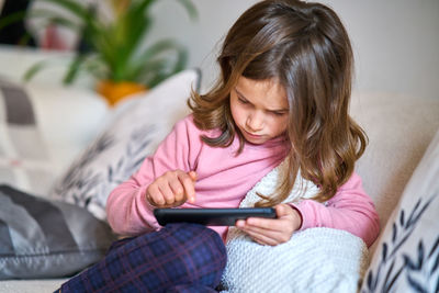 Girl looking away while sitting on sofa at home