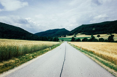 Road amidst agricultural field against sky