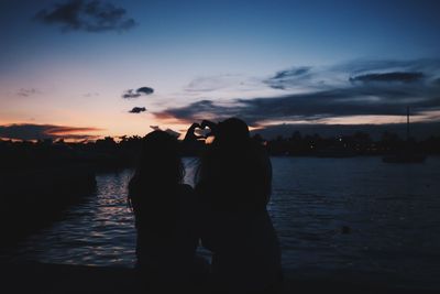 Silhouette woman standing by lake against sky during sunset