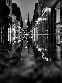 Wet street with reflection amidst illuminated buildings in city