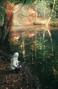 Rear view of woman sitting on lakeside in forest