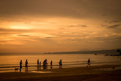 Silhouette people playing on beach against sky during sunset