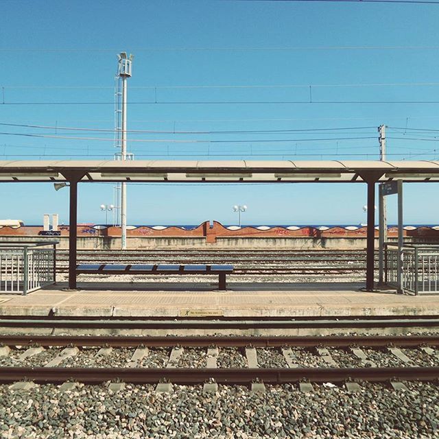 railroad track, rail transportation, power line, transportation, railroad station platform, public transportation, railroad station, built structure, architecture, cable, electricity pylon, connection, clear sky, building exterior, power supply, train - vehicle, sky, electricity, railway track, blue