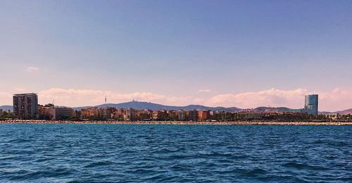 Sea by cityscape against blue sky