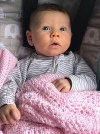 Portrait of cute baby girl sitting on bed at home