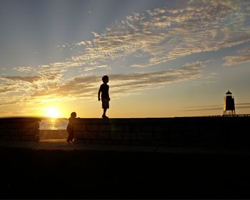 Silhouette of man overlooking calm sea at sunset