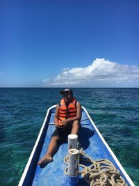 Full length of man sitting in sea against blue sky