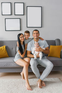 Happy family with two children are sitting on the sofa in their house and smiling person