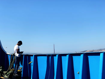 Man standing by railing against clear blue sky