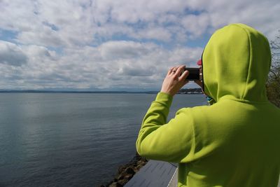 Rear view of man photographing sea against sky