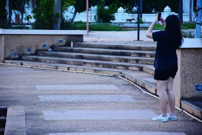 Rear view of woman photographing on road