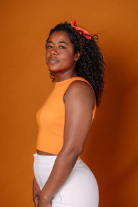 Side view of young woman looking away while standing against yellow background