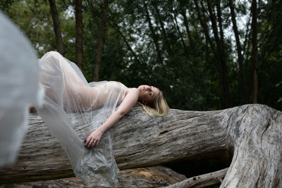 Portrait of naked woman wrapped in a polythene lying down on tree trunk in forest