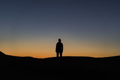 Rear view of silhouette man standing on land against clear sky during sunset