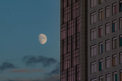 Moon rising behind a half-glass and half-concrete building