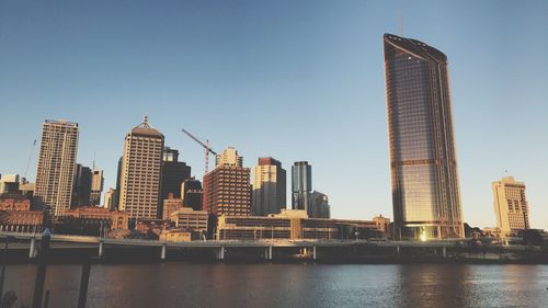 Skyscrapers by river against clear sky