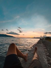 Low section of man relaxing by sea against sky during sunset