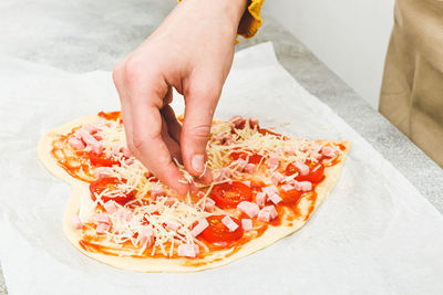 Hand of caucasian teenage girl pouring grated cheese on pizza hearts .