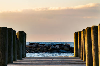 Wooden posts on beach by sea against sky during sunset