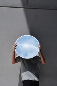 Man holding circle shaped mirror while standing against wall