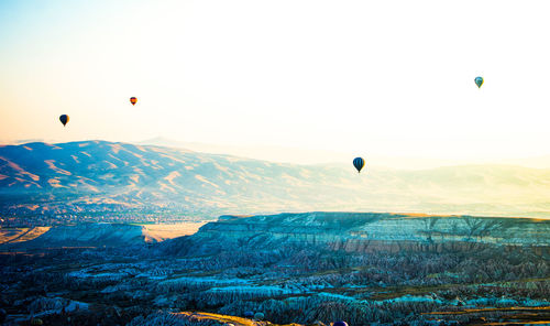 Hot air balloons flying over mountains against clear sky