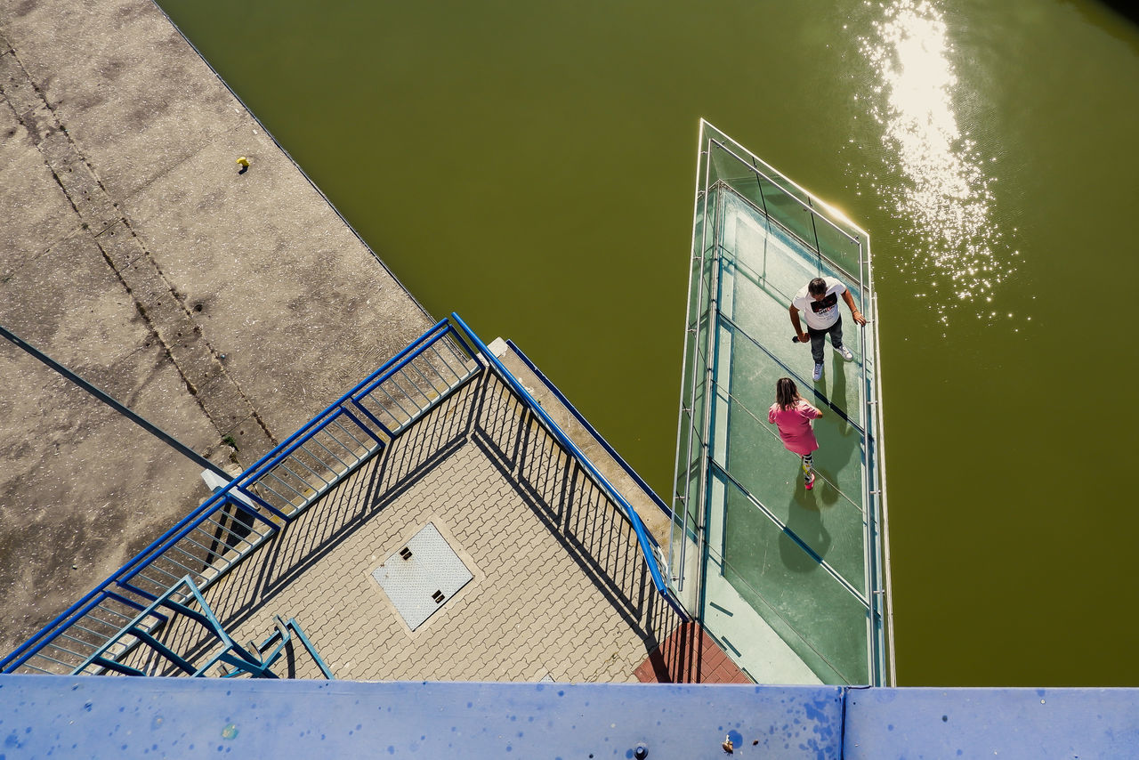 HIGH ANGLE VIEW OF PEOPLE BY LAKE AGAINST METAL STRUCTURE