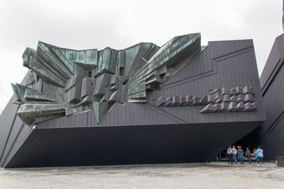 People standing by building in city against sky