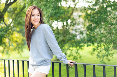 Portrait of smiling young woman standing against railing