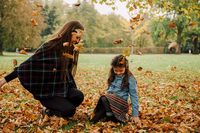 Young woman and little girl playing with autumn leaves on a meadow