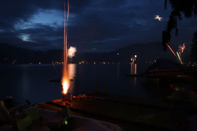 Fireworks exploding on pier by lake at night