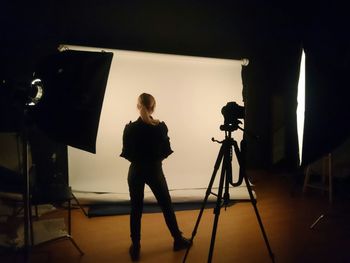 Full length rear view of woman standing by tripod in studio