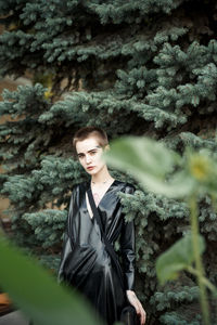 Portrait of young woman standing against tree