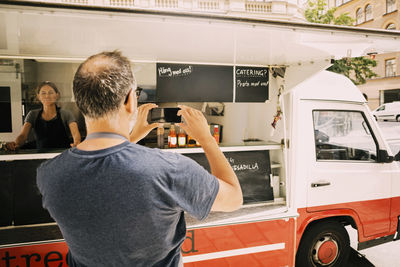 Rear view of owner photographing street food truck in mobile phone