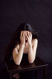 Portrait of young woman sitting against black background