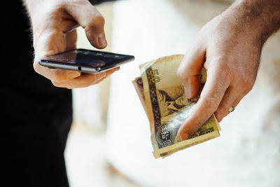 Cropped image of man using smart phone while holding paper currency