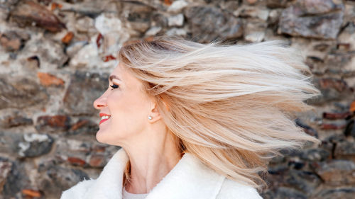 Radiant senior lady with windswept blonde hair against rough stone texture