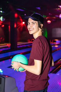 Portrait of smiling teenage boy holding ball at bowling alley