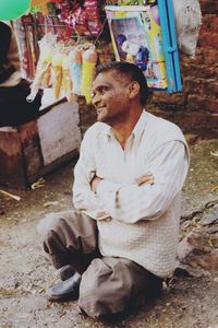 Smiling mature man with arms crossed looking away while sitting in market