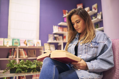 A young girl is sitting reading a book with a purple background