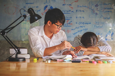 Friends studying at desk against whiteboard